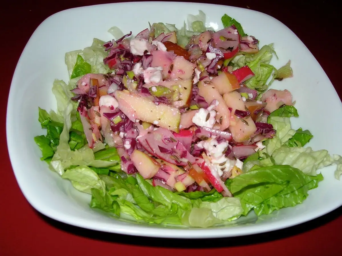 Plato de ensalada con lechuga, lombarda y trozos de manzana sobre un fondo rojo