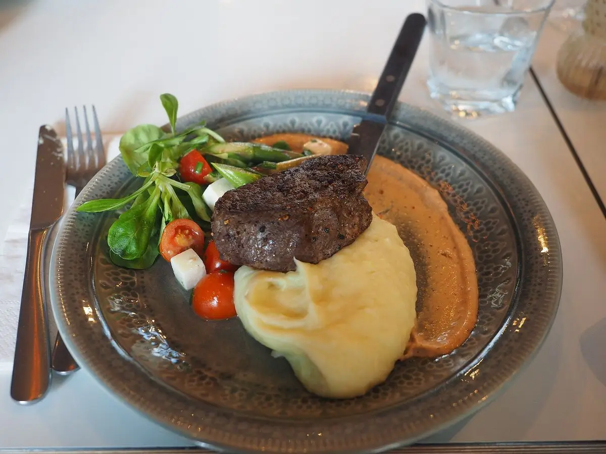 Filete de ternera con puré de patata, tomate y hojas verdes en un plato oscuro