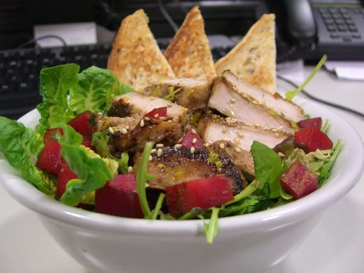 Cuenco de ensalada con hojas verdes, tomate, lonchas de carne de cerdo a la plancha y picatostes