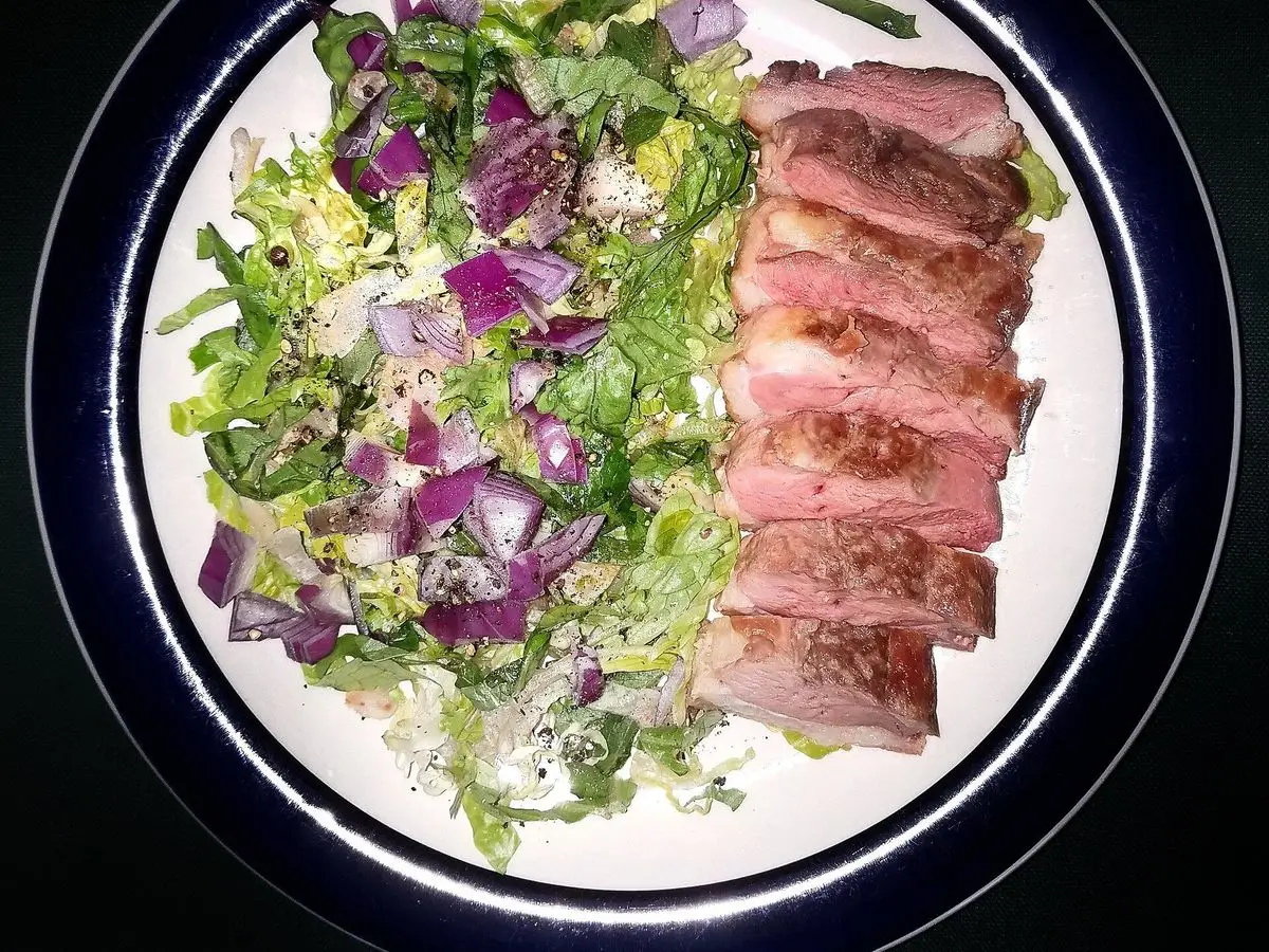 Plato con lonchas de pechuga de pato sobre ensalada de hojas verdes y cebolla morada