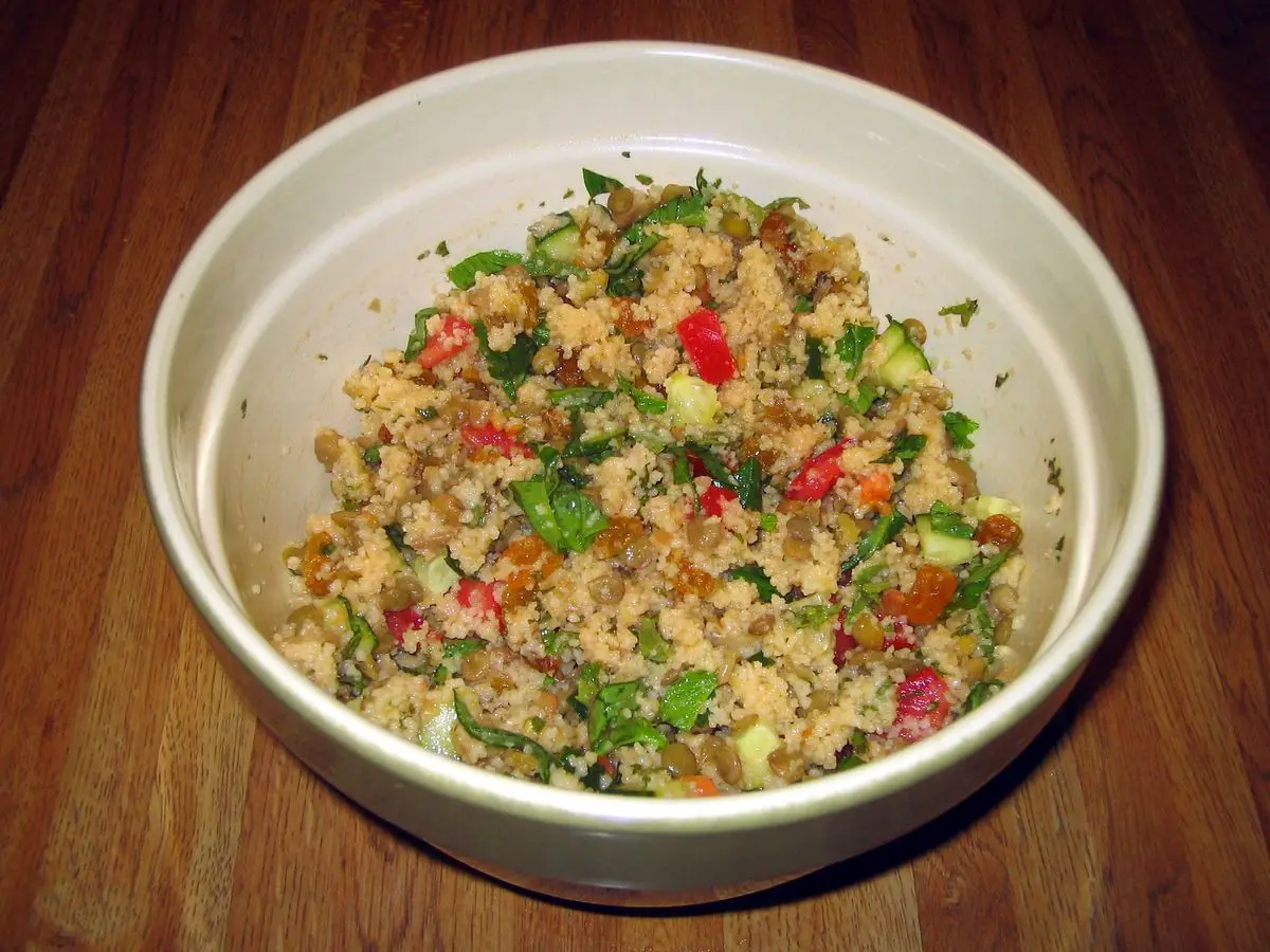 Cuenco blanco de ensalada de cuscús con hierbas picadas y trocitos de pimiento rojo