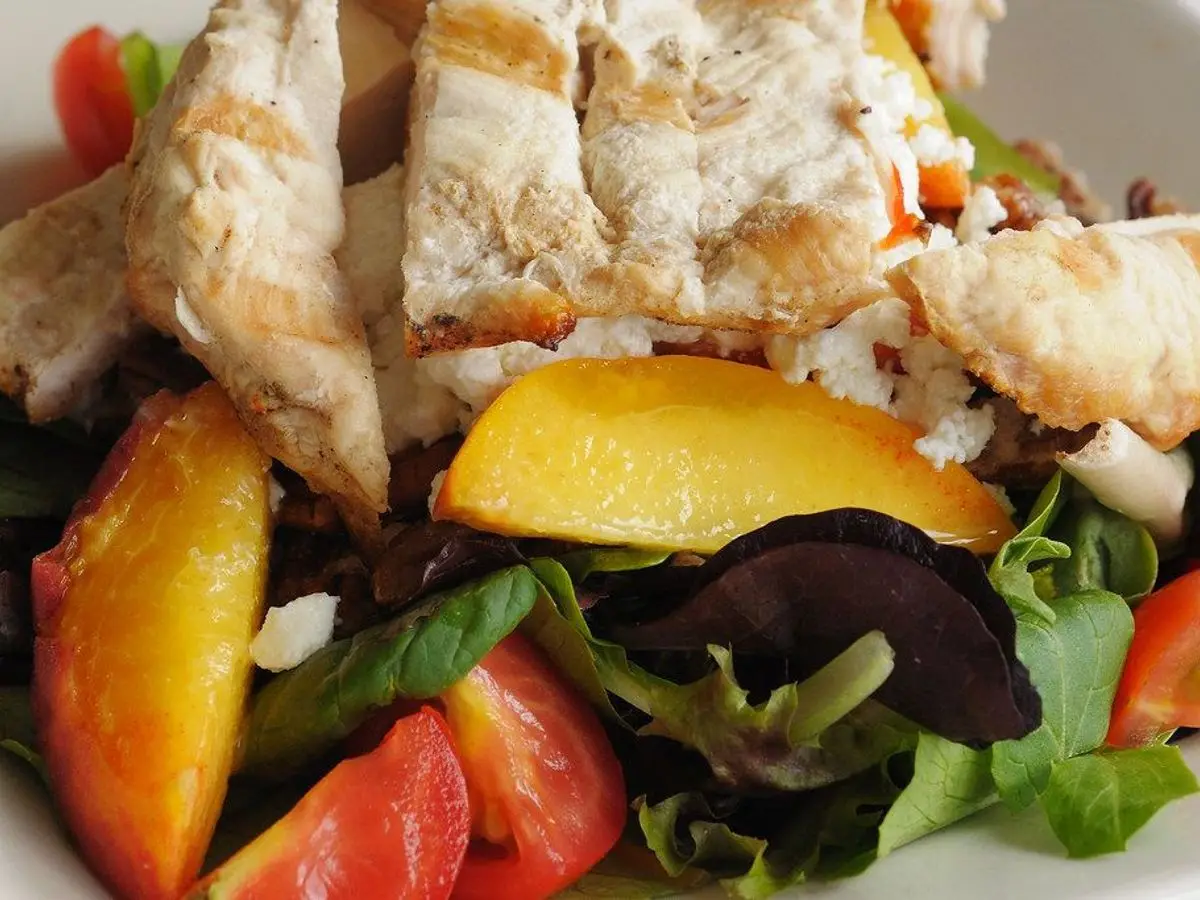 Ensalada con tiras de pechuga de pollo, gajos de melocotón, tomate y hojas verdes variadas