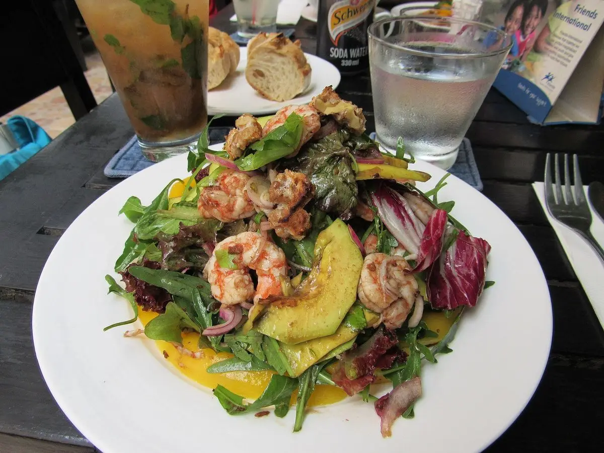 Ensalada de gambas con aguacate, naranja, lechugas moradas y hojas verdes en un plato blanco