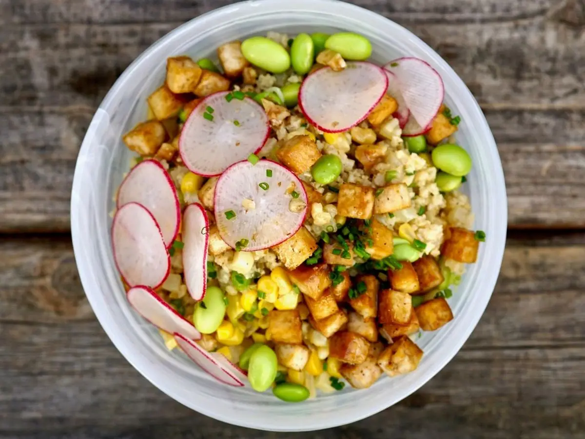Cuenco de ensalada de granos con rabanitos en rodajas, edamame, maíz y taquitos crujientes