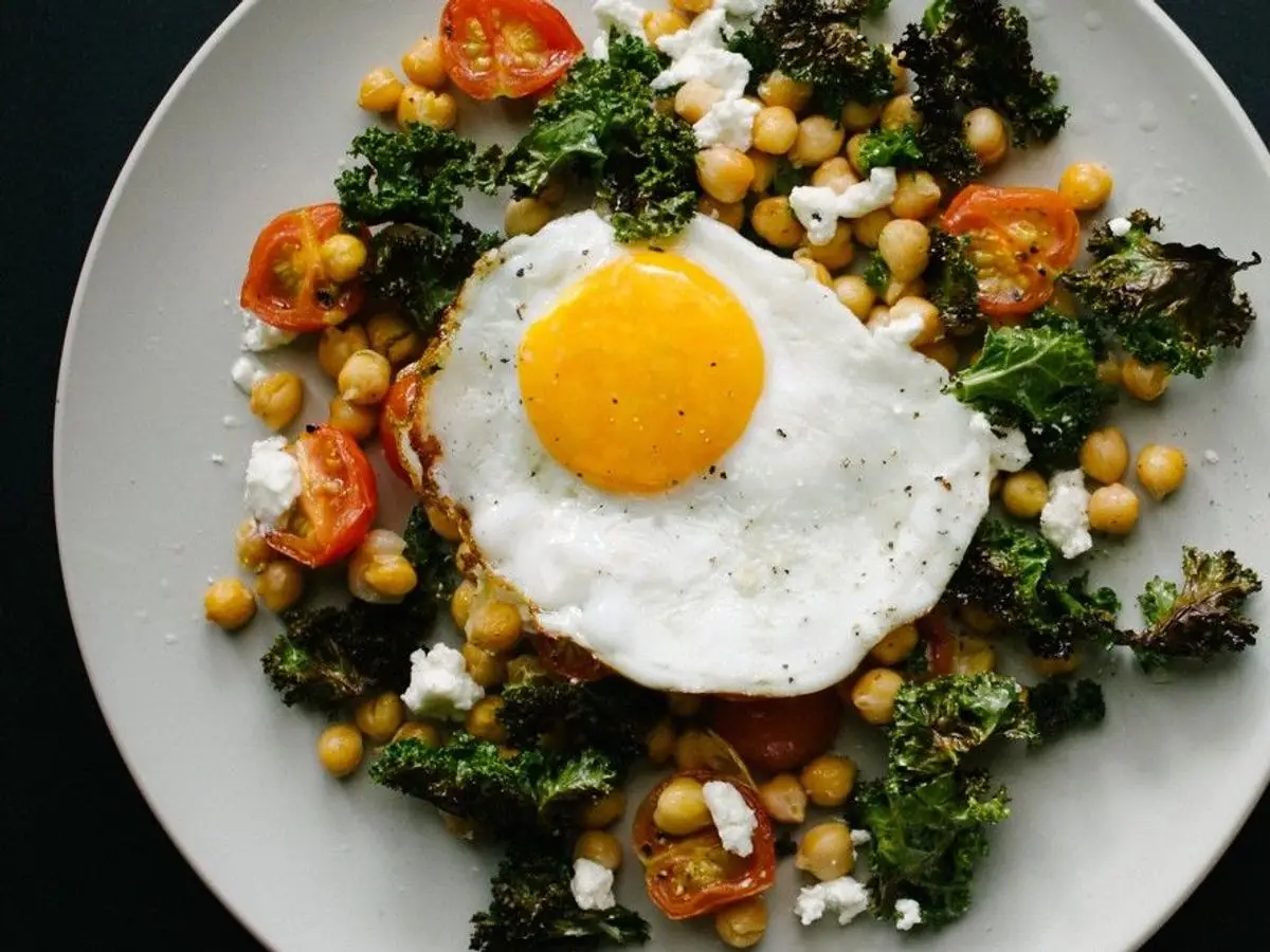 Ensalada de garbanzos con huevo frito, tomate cherry y verdura de hoja verde en un plato blanco
