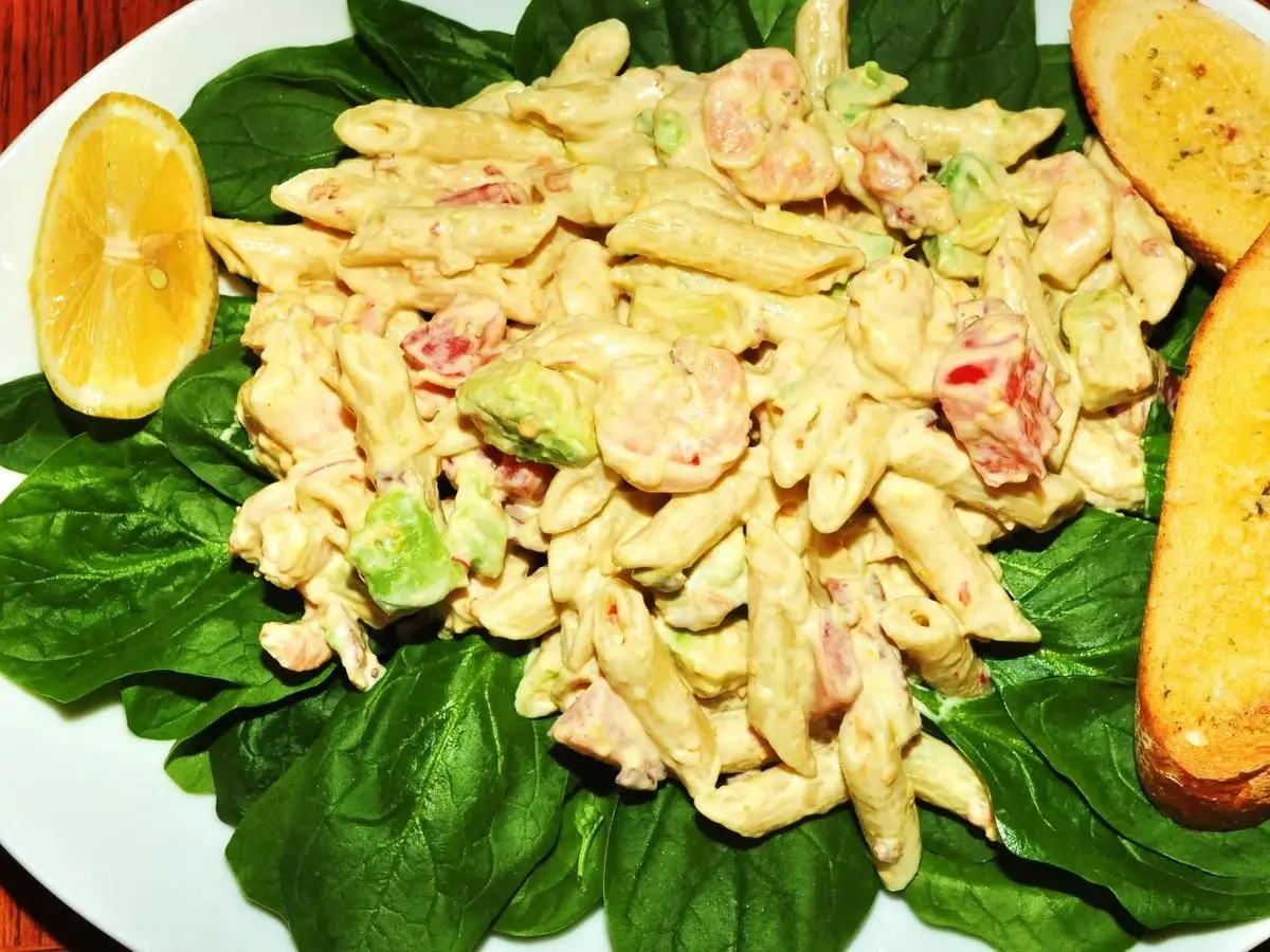 Ensalada de pasta con langostinos, aguacate y tomate sobre hojas verdes, con pan tostado y limón