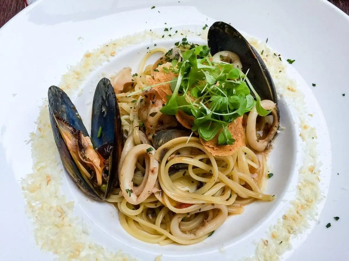 Espaguetis con calamar, mejillones y hojas verdes en un plato blanco hondo