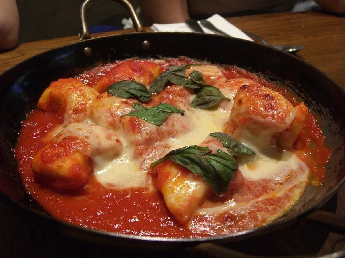 Sartén con ñoquis gratinados con mozzarella derretida, salsa de tomate y hojas de albahaca