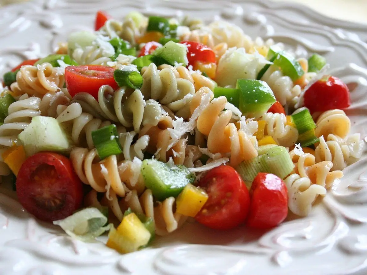 Ensalada de pasta fusilli con tomate cherry, pimiento verde y amarillo y verduras picadas en un plato blanco