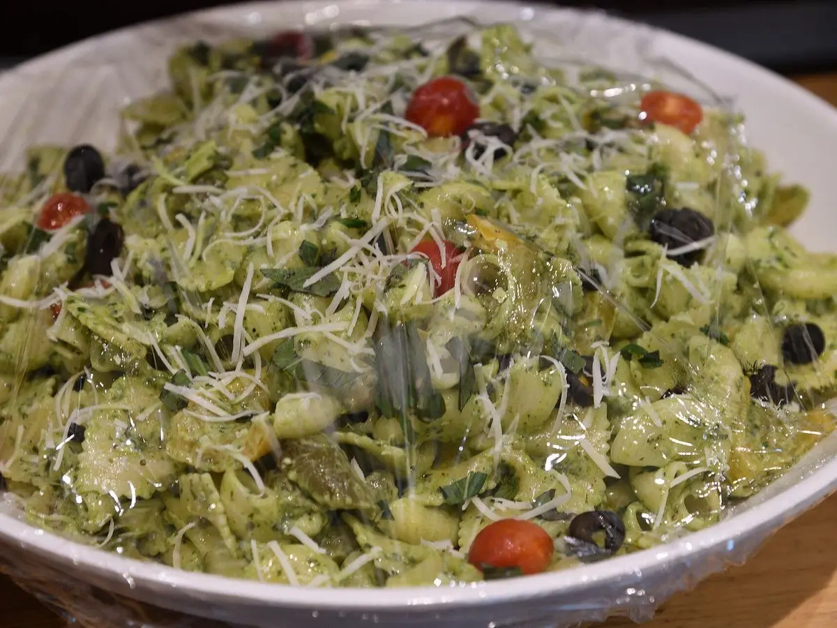 Fuente de pasta con pesto verde, tomates cherry, aceitunas negras y queso rallado