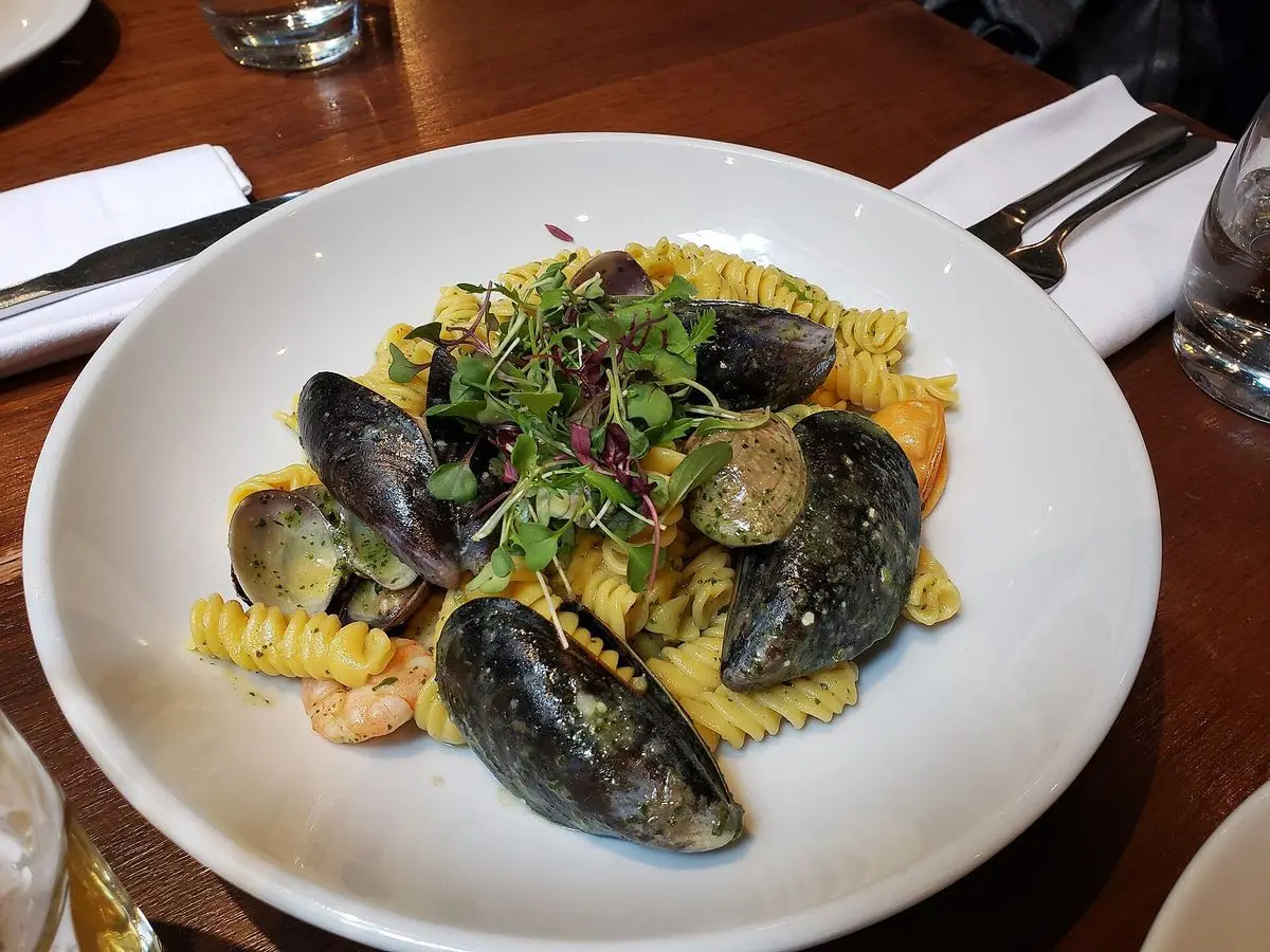 Plato hondo con pasta, mejillones abiertos y hierbas frescas por encima