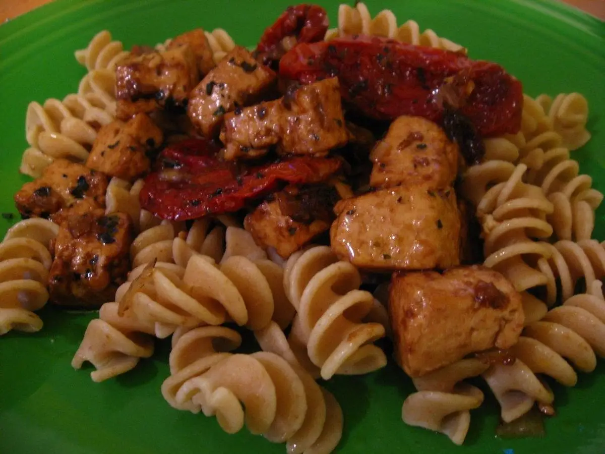 Espirales de pasta integral con tacos de pollo o pavo salteado y tomates secos sobre un plato verde