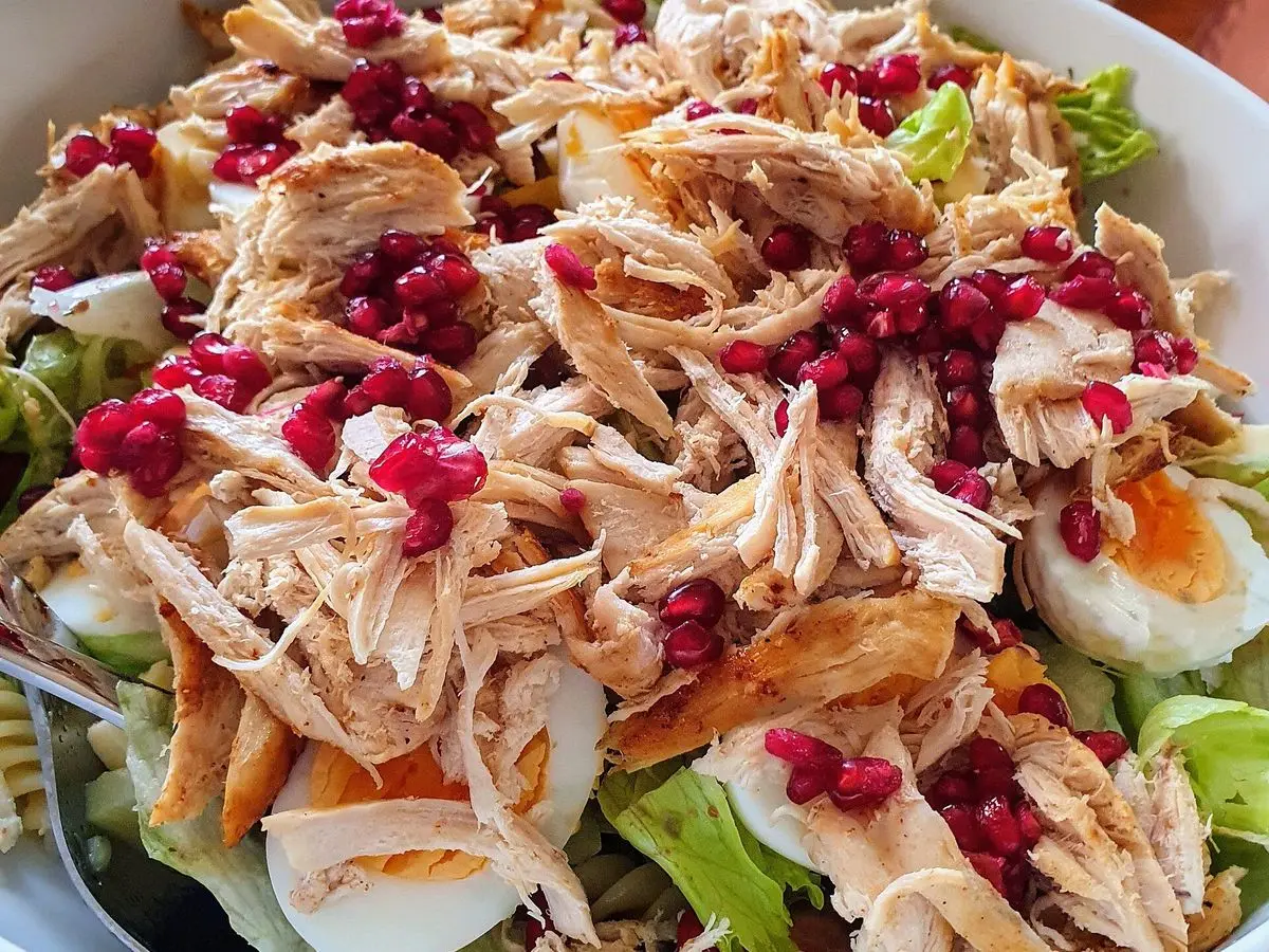 Ensalada de pollo desmenuzado con huevo cocido, zanahoria, hojas verdes y granos de granada