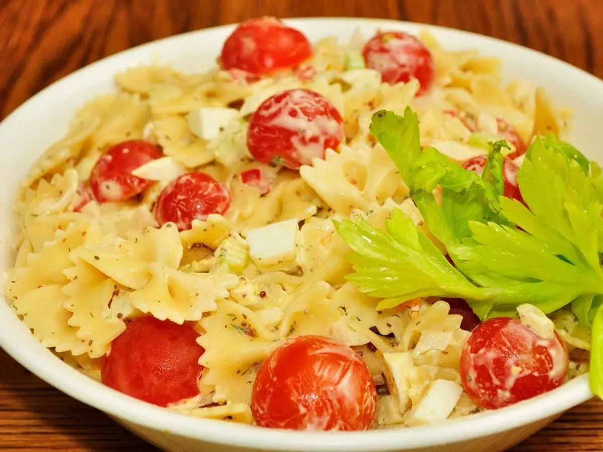 Cuenco blanco de pasta de lazos con tomates cherry, apio y queso, ensalada fría