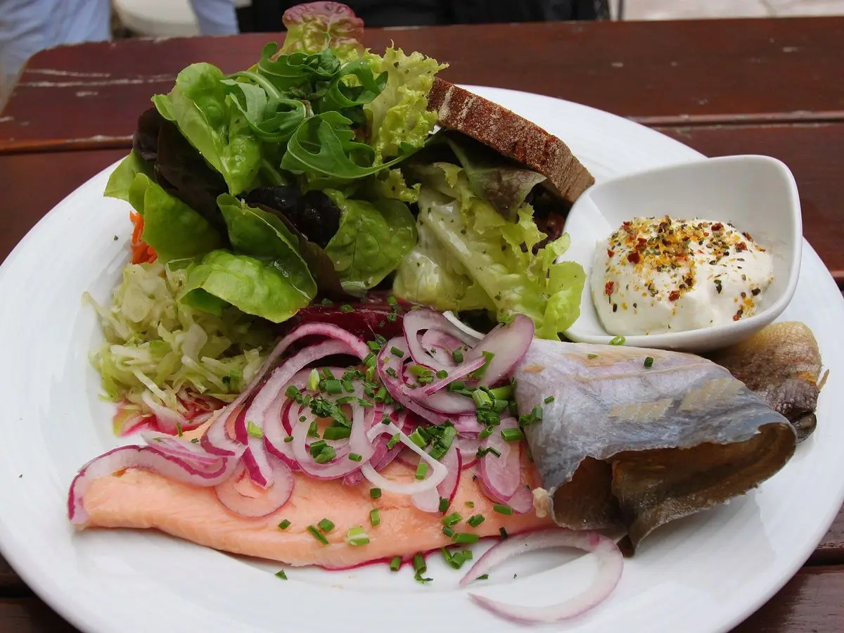 Plato con pescado ahumado, cebolla morada en tiras, hojas verdes y salsa blanca