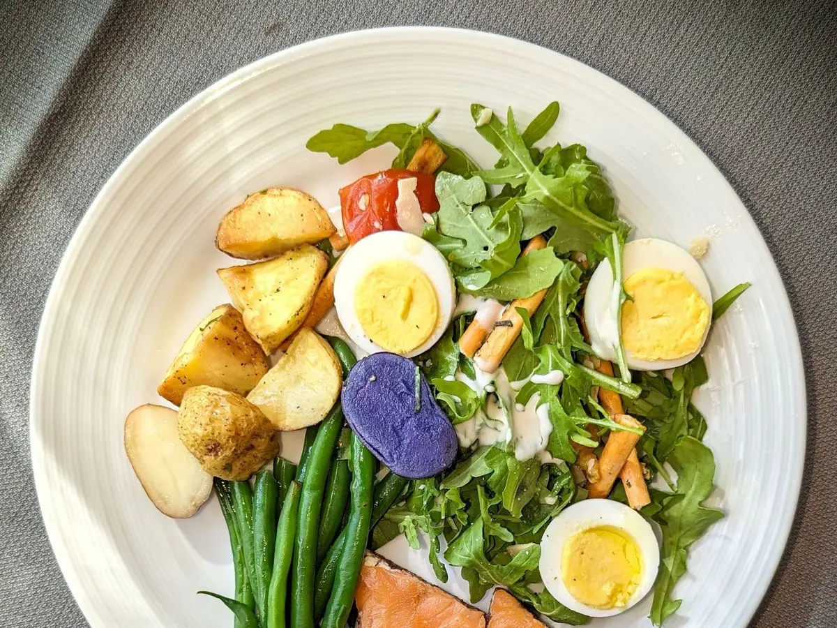Ensalada con patatas moradas y amarillas, huevo cocido, judías verdes, rúcula y tomate en un plato blanco