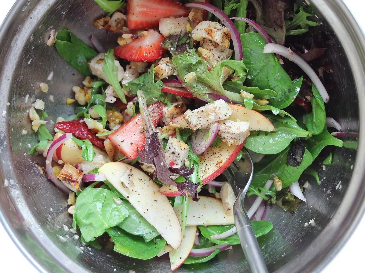 Cuenco con ensalada de espinacas, fresas, pollo, nueces y cebolla morada
