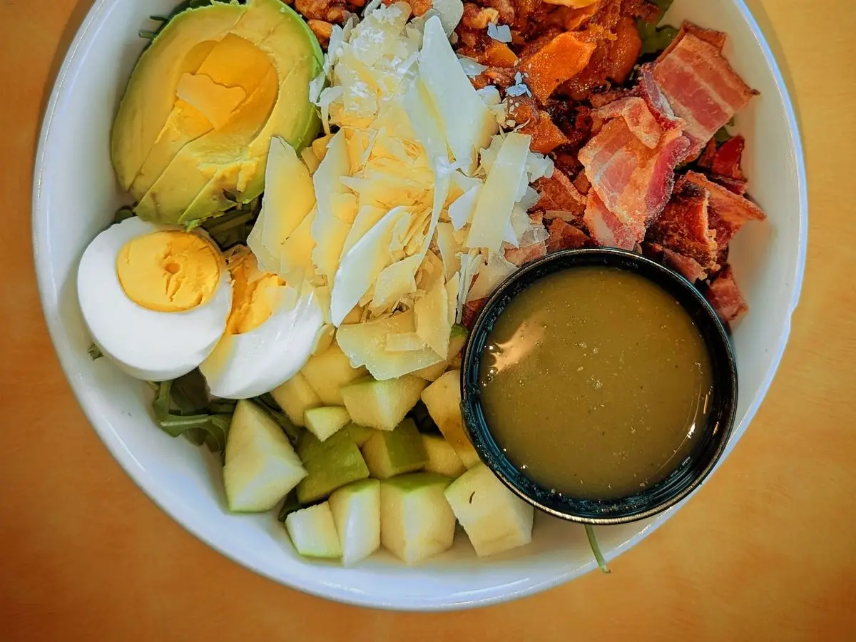 Ensalada en cuenco con huevo duro, aguacate, beicon, pollo y lechuga con salsa a un lado
