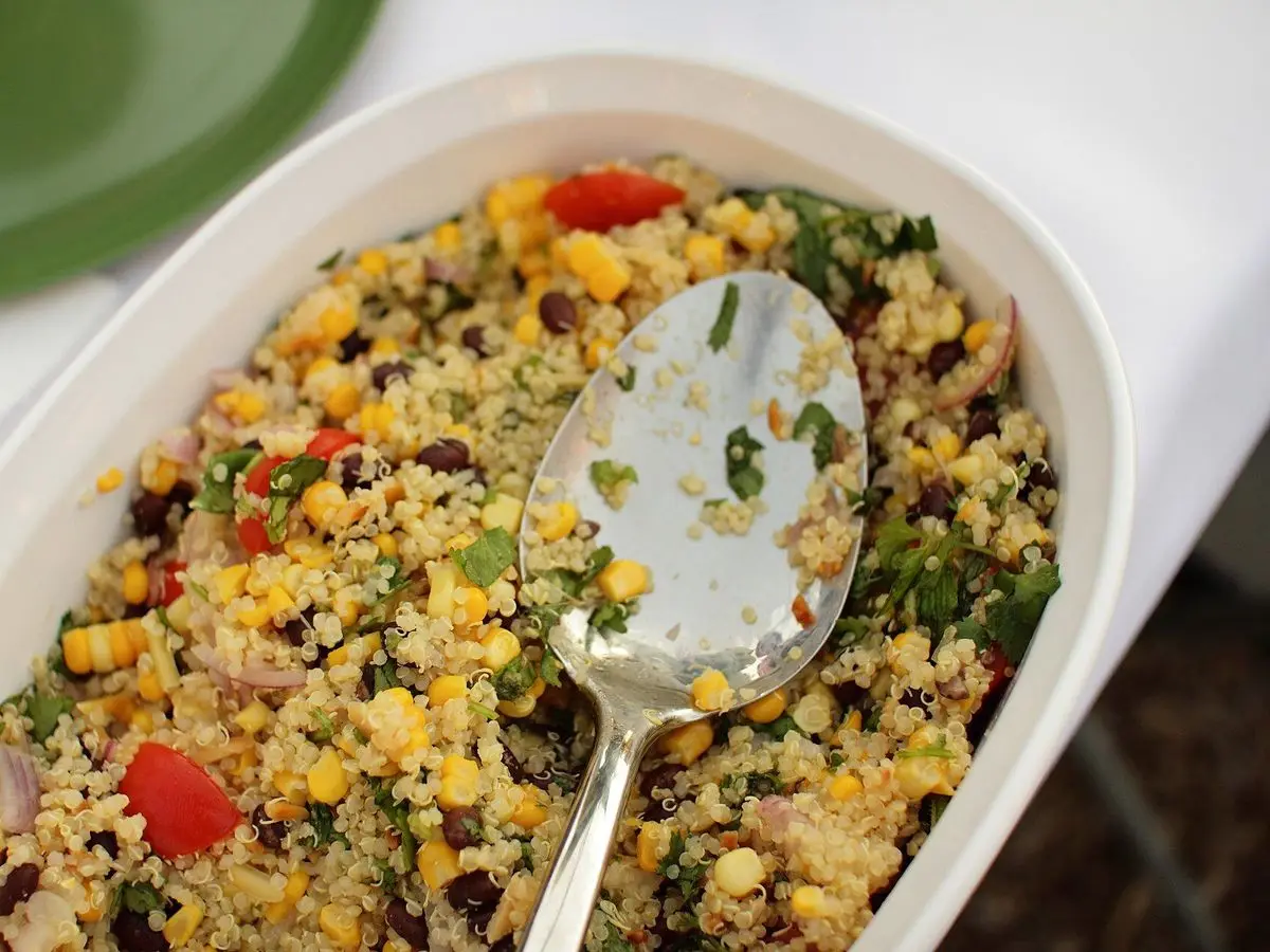 Fuente blanca con ensalada de quinoa, maíz, tomate, hierbas y alubias negras con una cuchara