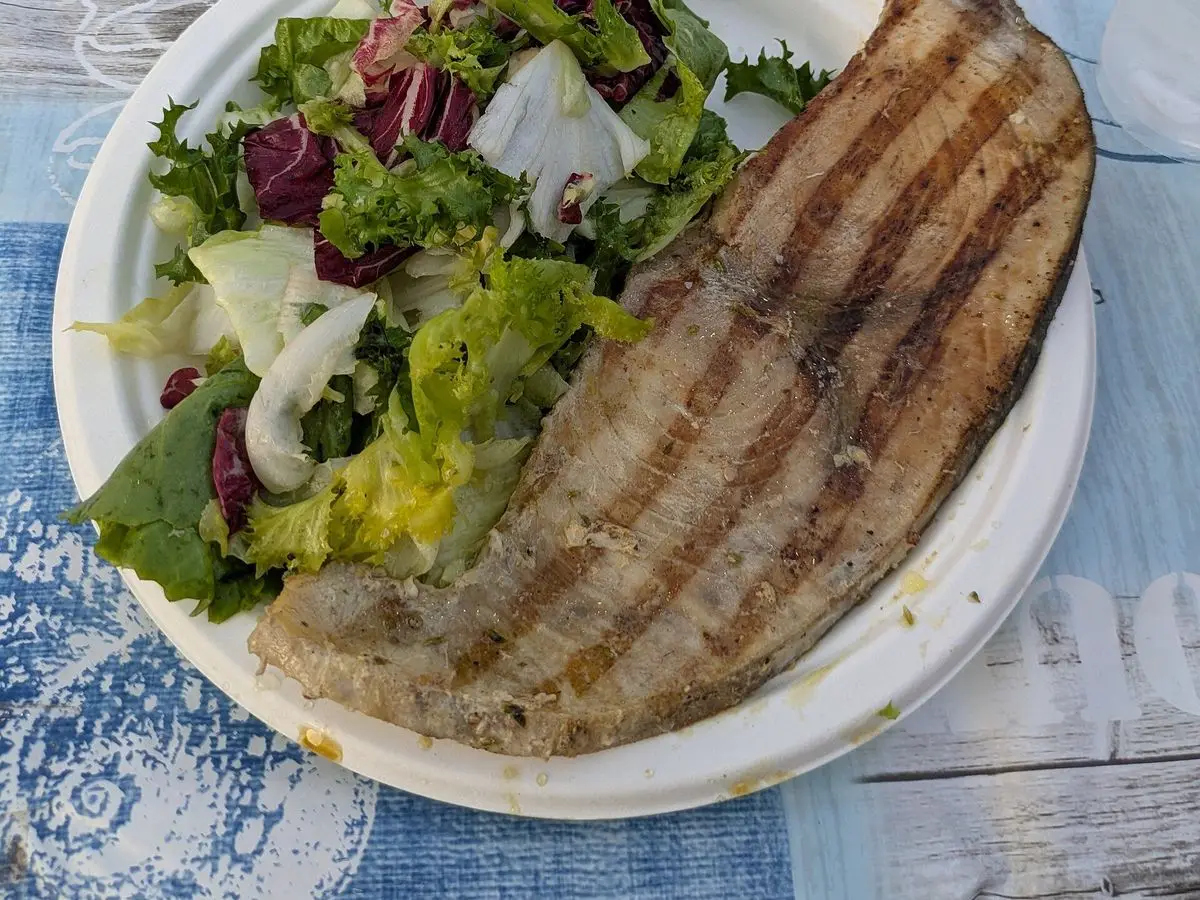 Filete de pescado a la plancha con ensalada de lechuga, cebolla y hojas moradas en plato blanco