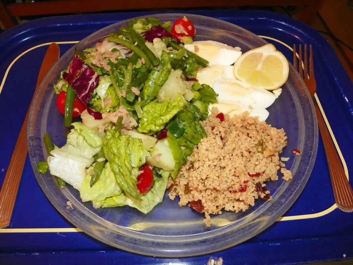 Plato con ensalada de lechugas, cuscús, huevo duro y rodaja de limón sobre mantel azul