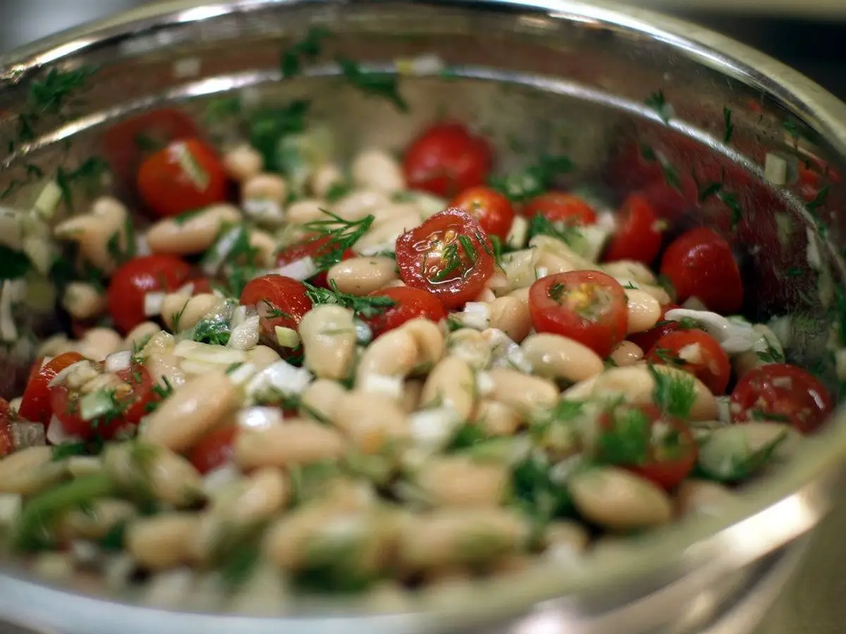 Cuenco metálico de ensalada de alubias blancas con tomates cherry y hierbas