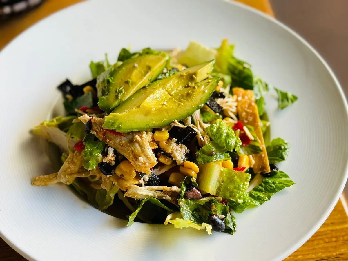 Ensalada verde con pollo desmenuzado, aguacate en láminas y granos de maíz en un plato blanco