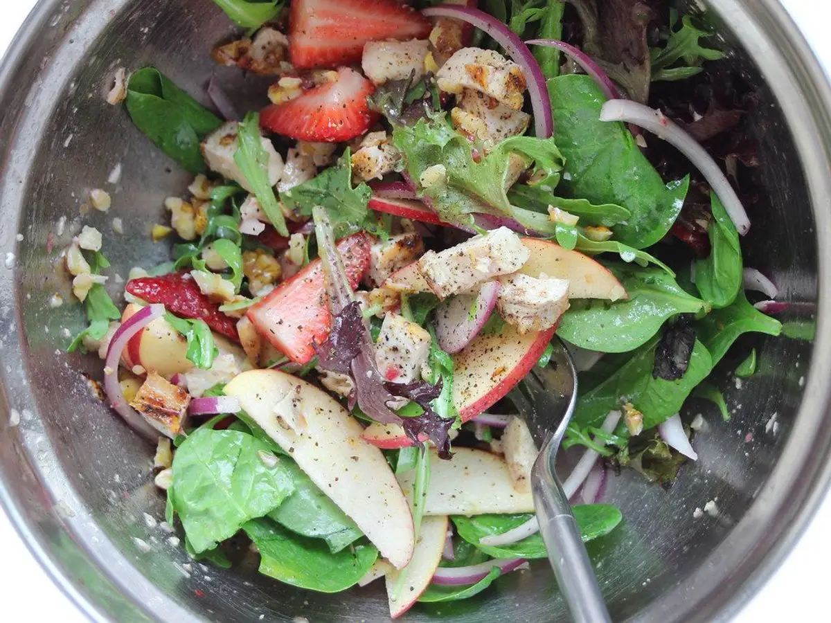 Ensalada de hojas verdes con pollo a la plancha, fresas, manzana, nueces y cebolla morada en un bol
