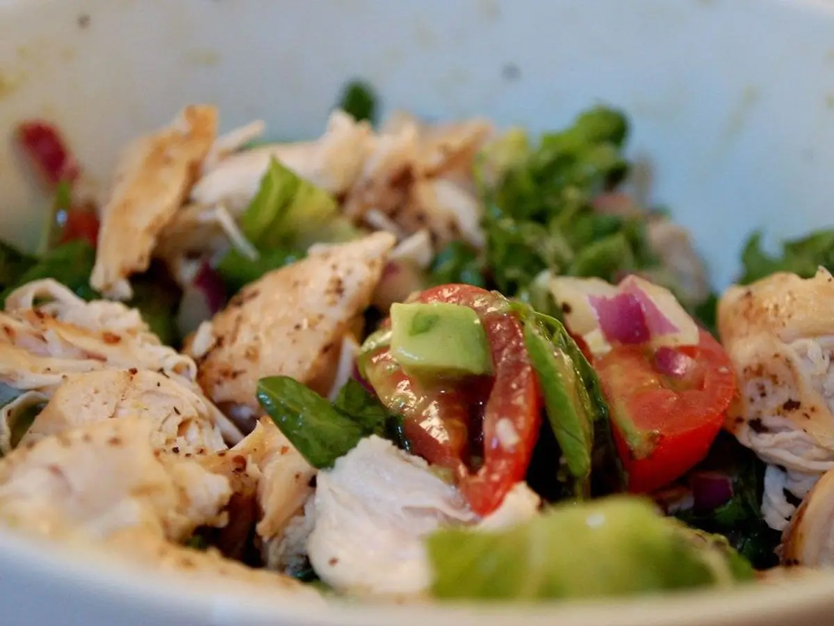 Cuenco de ensalada con pollo desmenuzado, tomate, aguacate, cebolla morada y hojas verdes