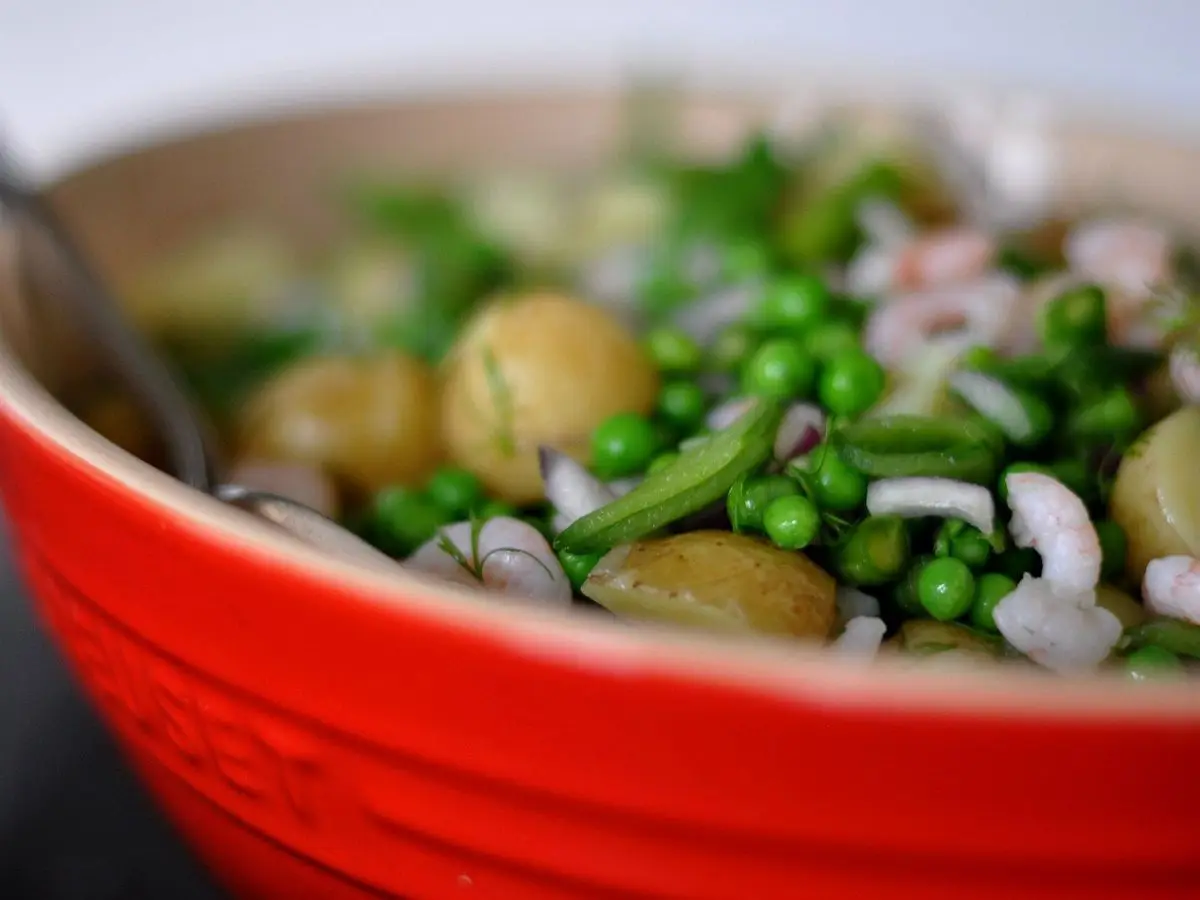 Cuenco rojo con ensalada de patatas nuevas, guisantes y hierbas frescas