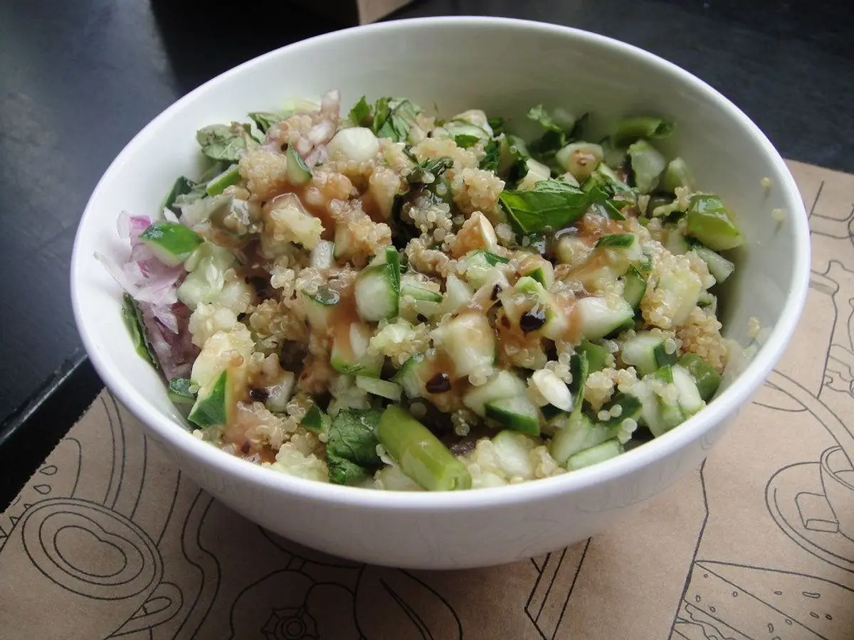 Bol blanco de ensalada de cereal con garbanzos, pepino y hierbas picadas