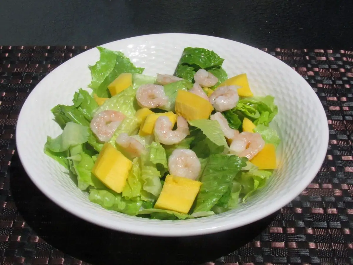 Ensalada de gambas cocidas, dados de mango y lechuga romana en un cuenco blanco