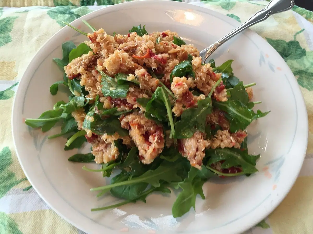 Ensalada de quinoa con tomate secado al sol sobre una cama de rúcula en un plato blanco