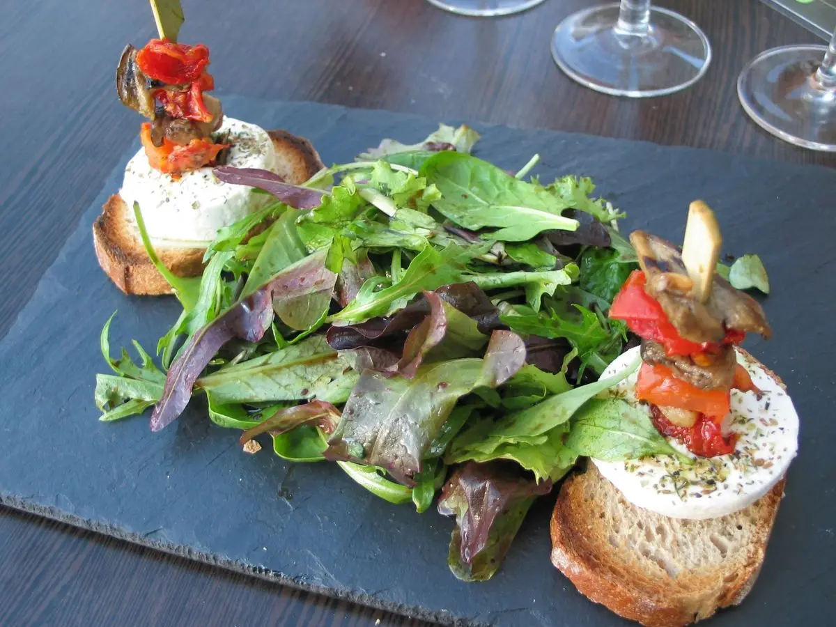 Pizarra con mezclum de hojas, tostadas de queso de cabra y brocheta de tomate