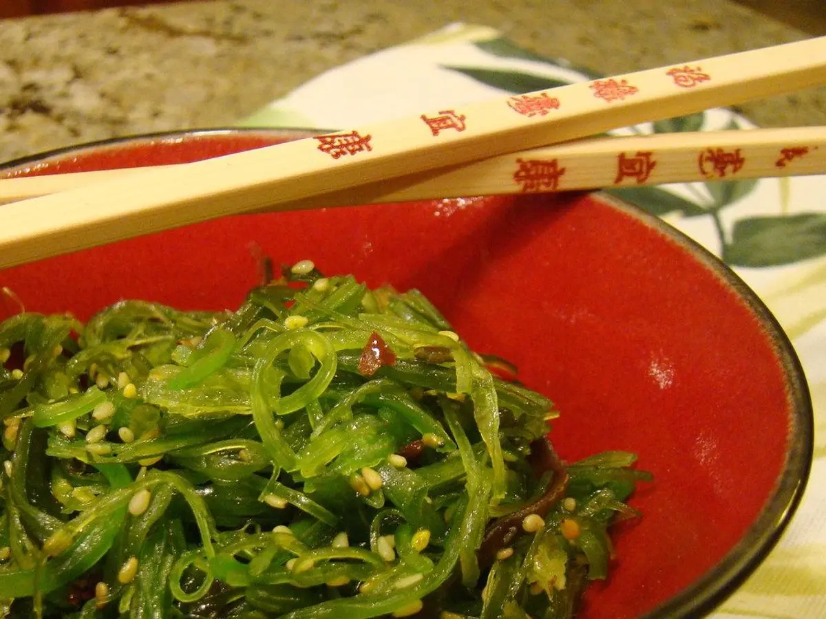 Cuenco rojo de ensalada de alga wakame con palillos