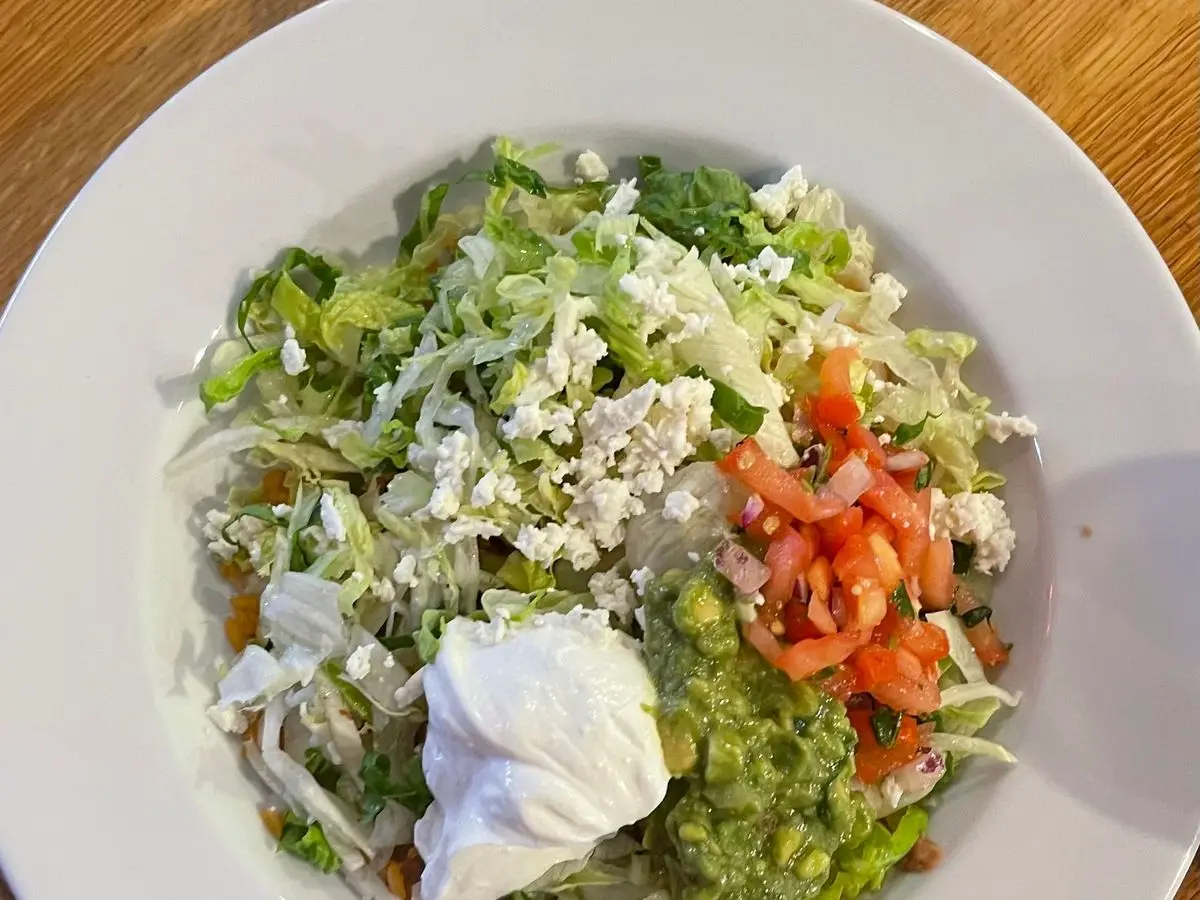 Plato blanco con ensalada estilo taco con lechuga, queso desmenuzado, tomate, guacamole y crema agria