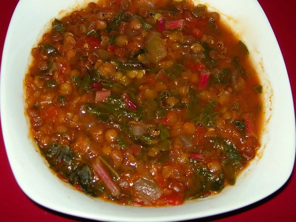 Plato hondo con guiso de lentejas y acelgas con tomate sobre un mantel rojo
