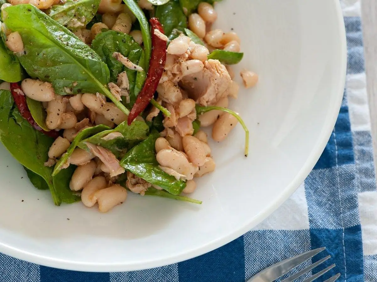 Plato blanco de ensalada de alubias blancas con hojas verdes de rúcula y espinaca