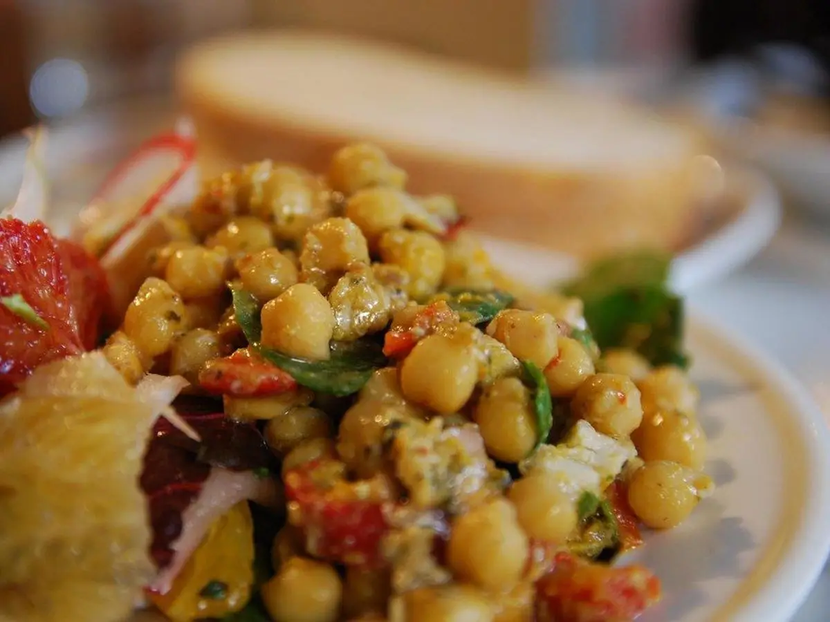 Plato con ensalada de garbanzos, tomate y rodajas de limón con pan al fondo