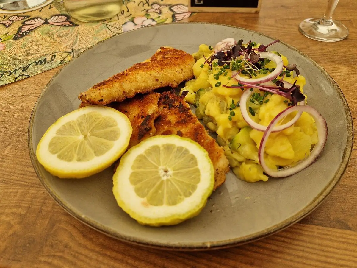 Filete de pescado empanado con ensalada templada de patata y cebolla morada y rodajas de limón