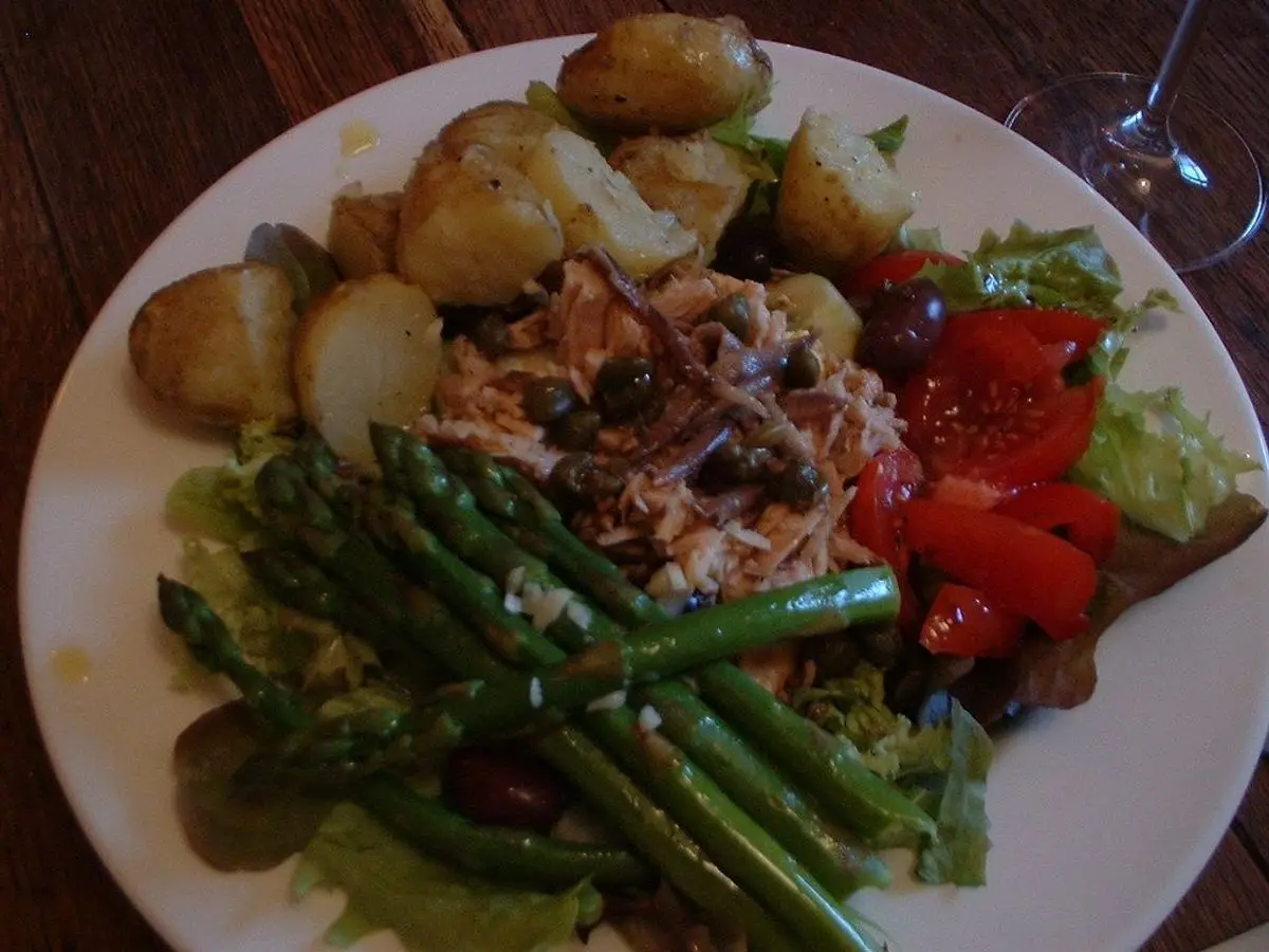Plato blanco con patatas, espárragos verdes, tomate y hojas verdes