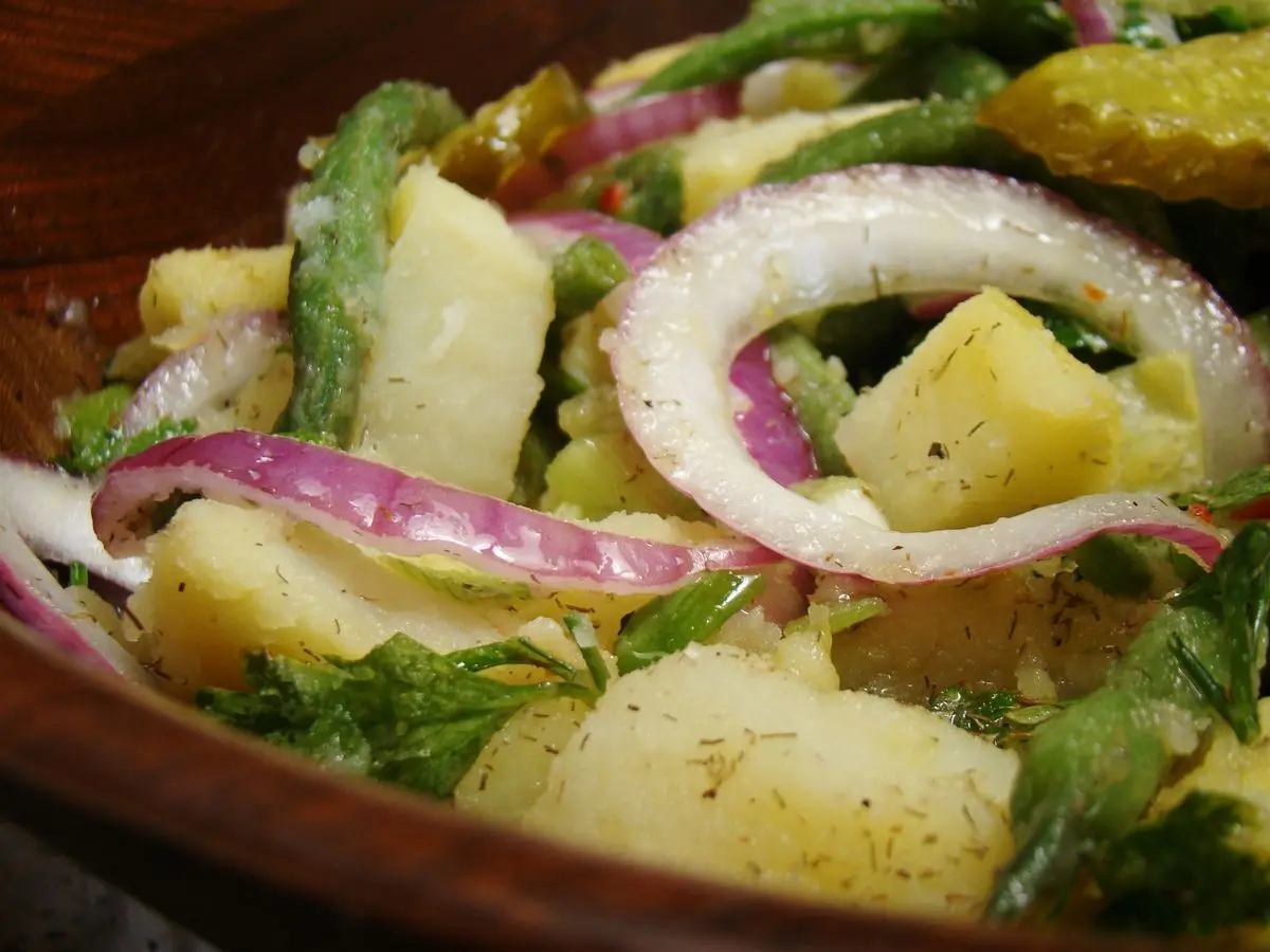 Ensalada de patata cocida, judías verdes, aros de cebolla morada, perejil y eneldo en una ensaladera de madera