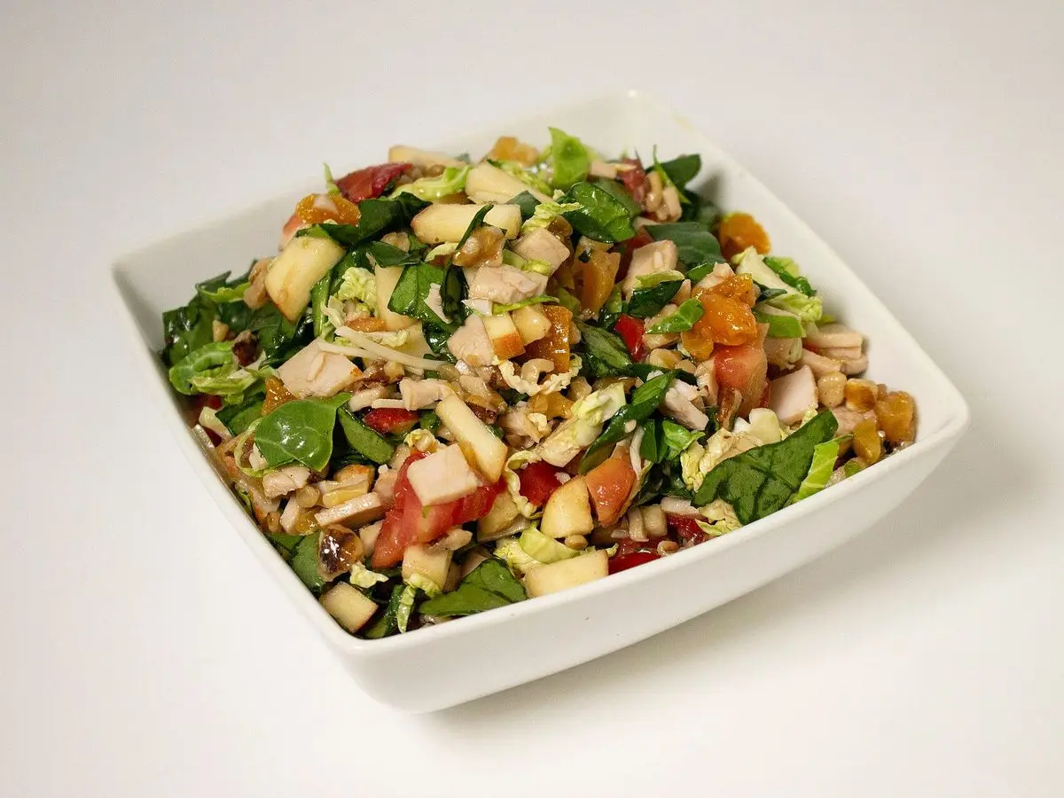 Ensalada en fuente blanca con carne en tiras, hojas verdes, tomate y frutos secos troceados