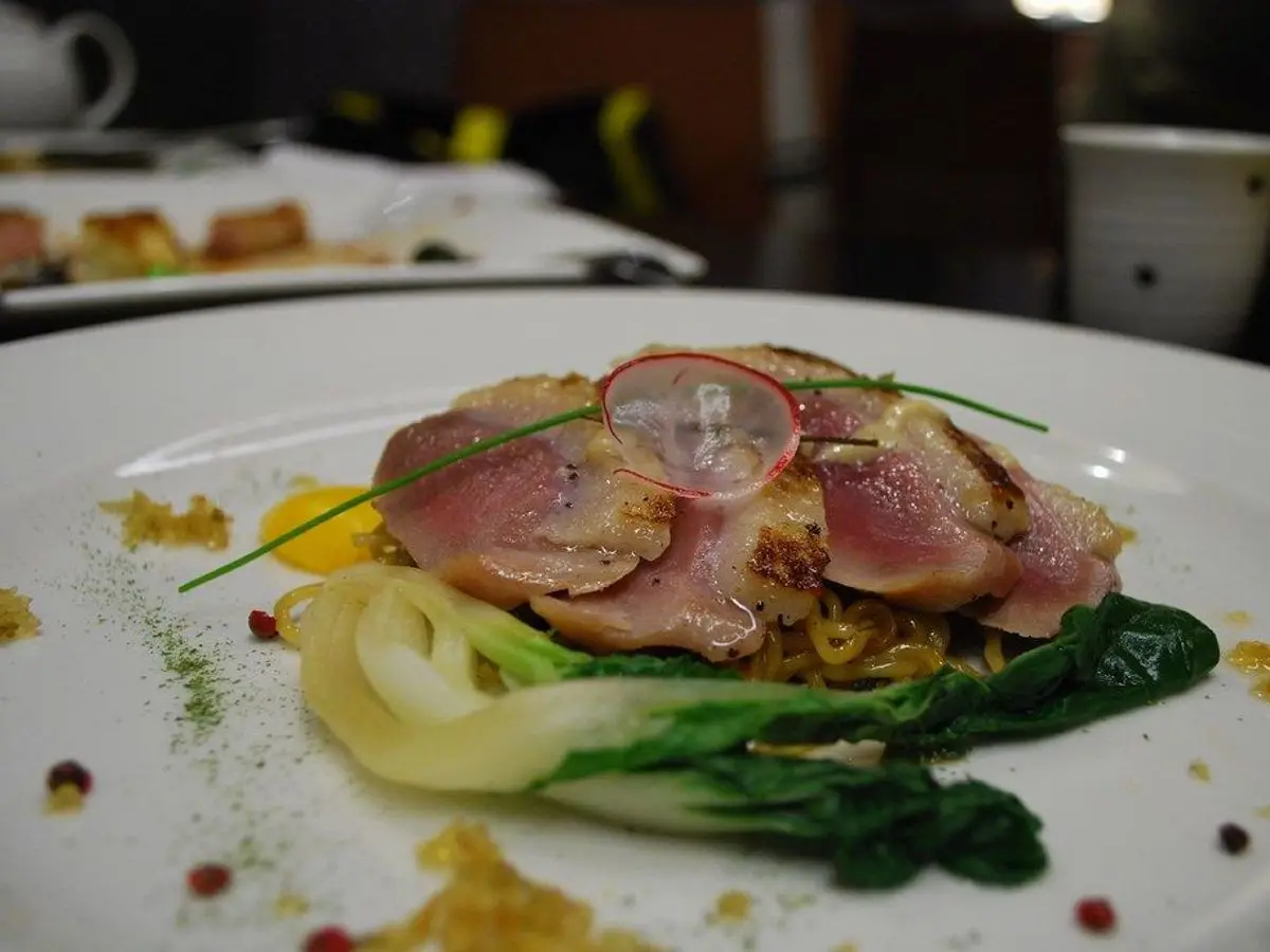 Lonchas de carne a la plancha sobre verduras de hoja salteadas en un plato blanco