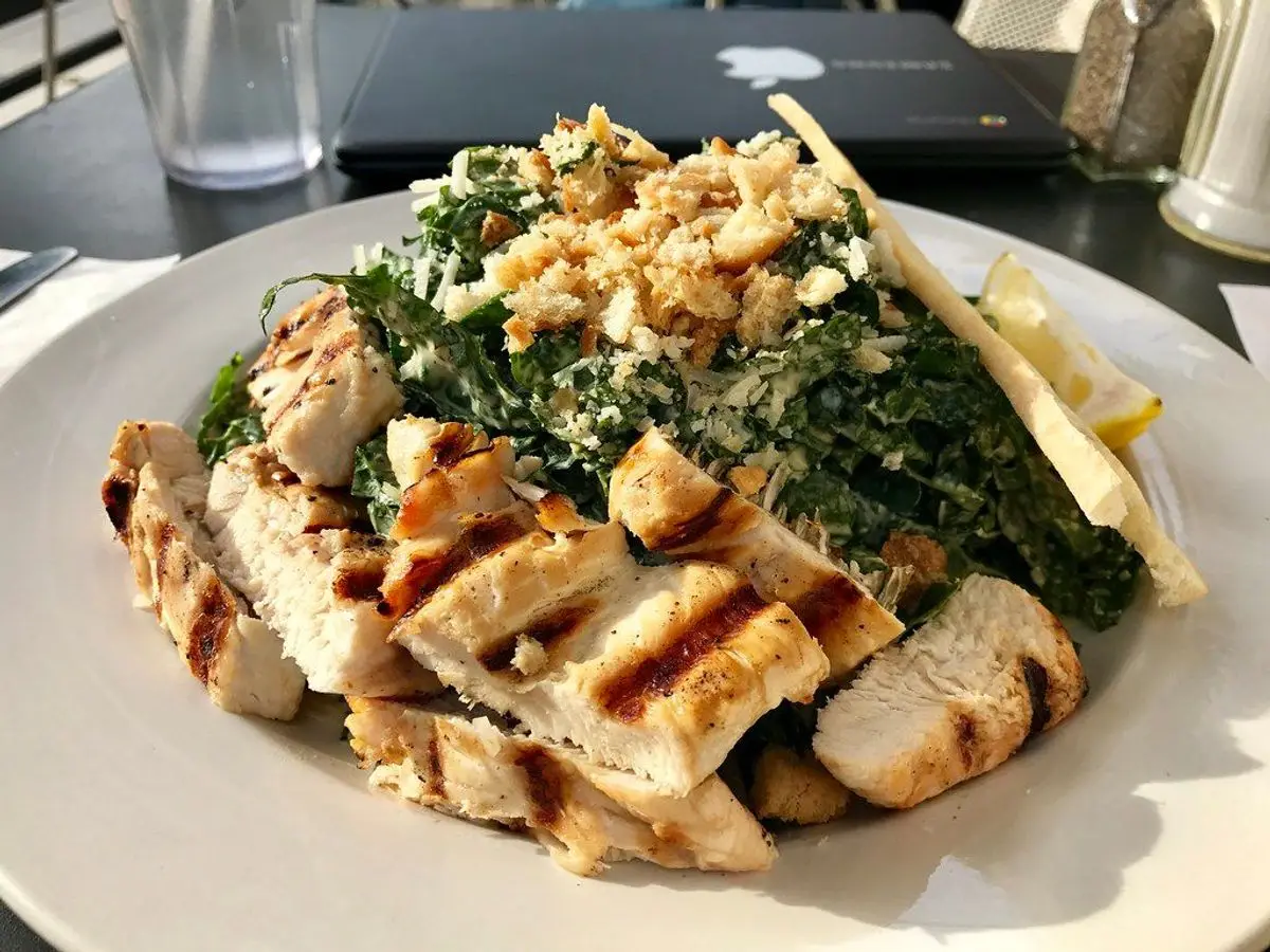Ensalada templada de col rizada con tiras de pechuga de pollo a la plancha y frutos secos por encima