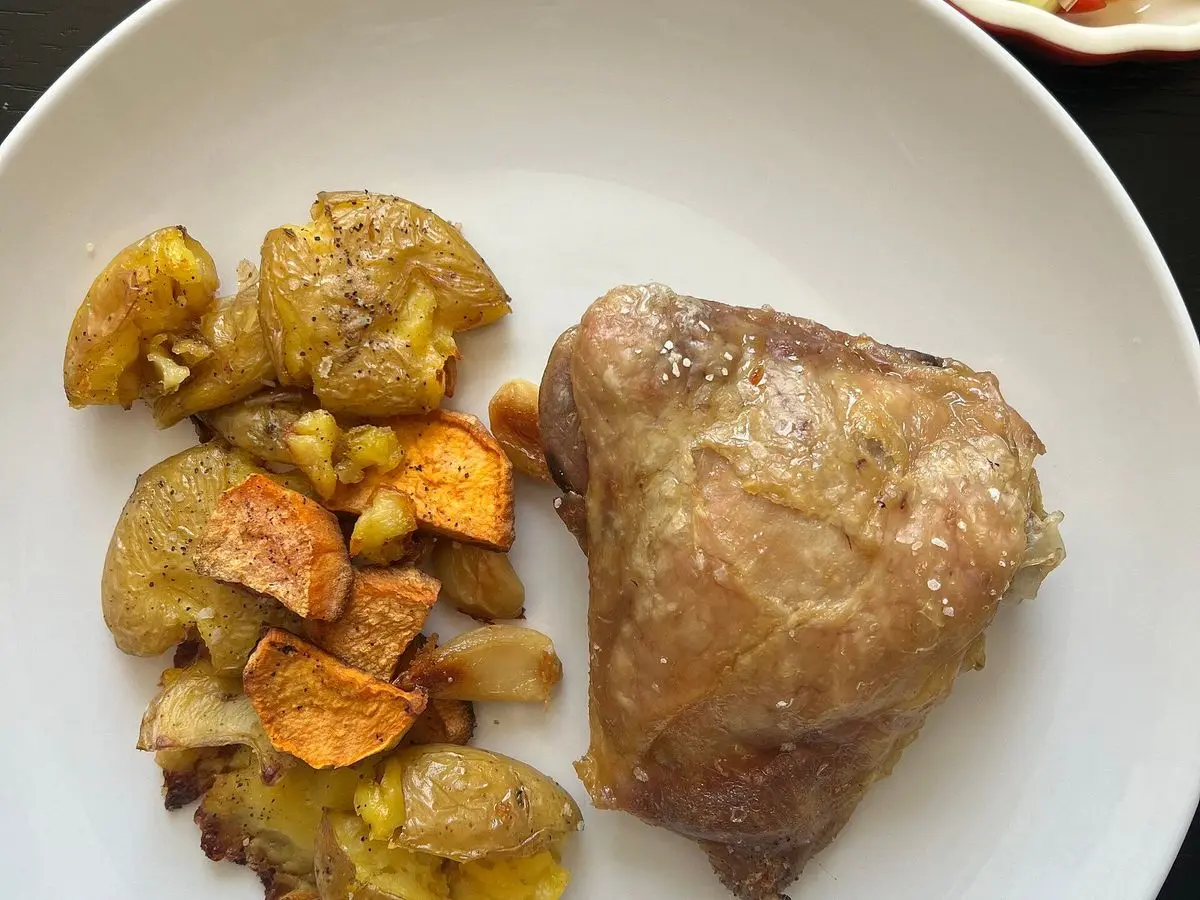 Muslo de pollo asado con patatas y boniato al horno en un plato blanco