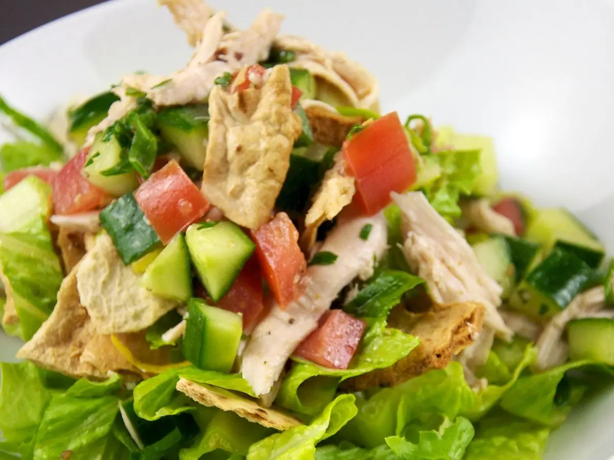Ensalada con tiras de pollo, lechuga, tomate, pepino y pimiento en un plato blanco