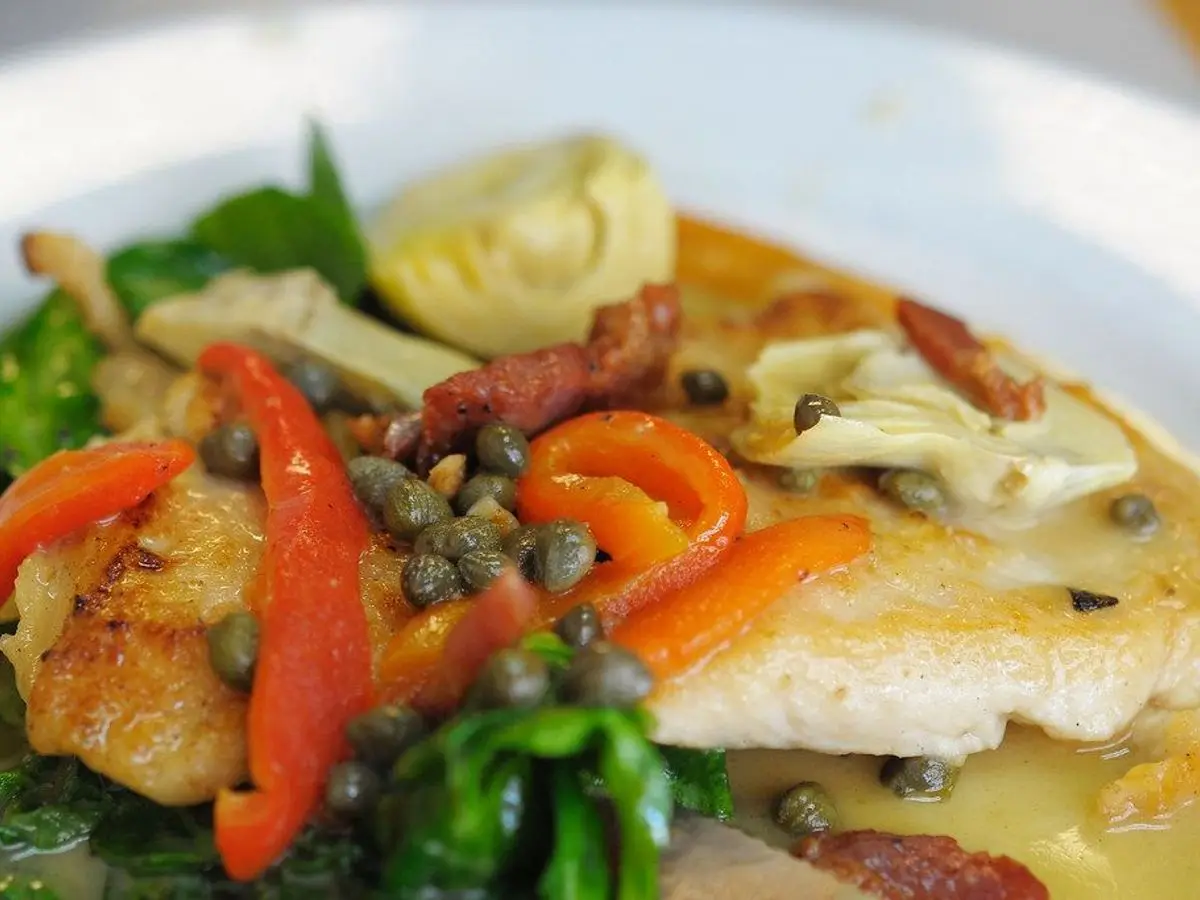 Filete de pescado blanco con alcachofas, tiras de pimiento y alcaparras en un plato