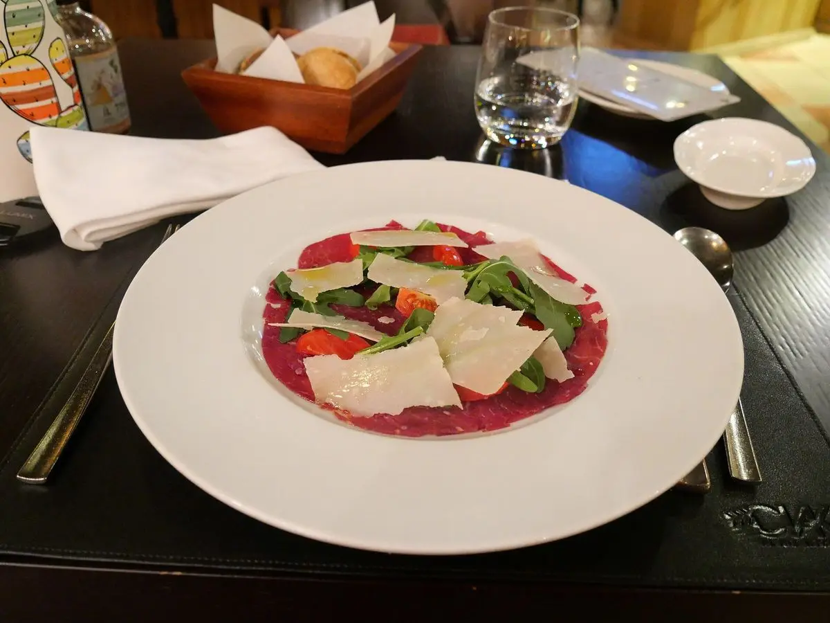 Plato blanco con carpaccio de ternera, rúcula, lascas de parmesano y tomate cherry