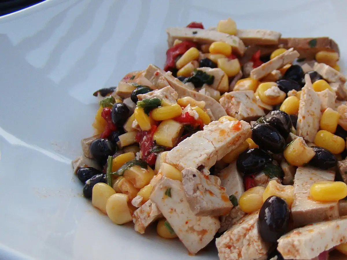 Ensalada de tofu en dados con maíz, alubias negras y pimiento en un plato blanco